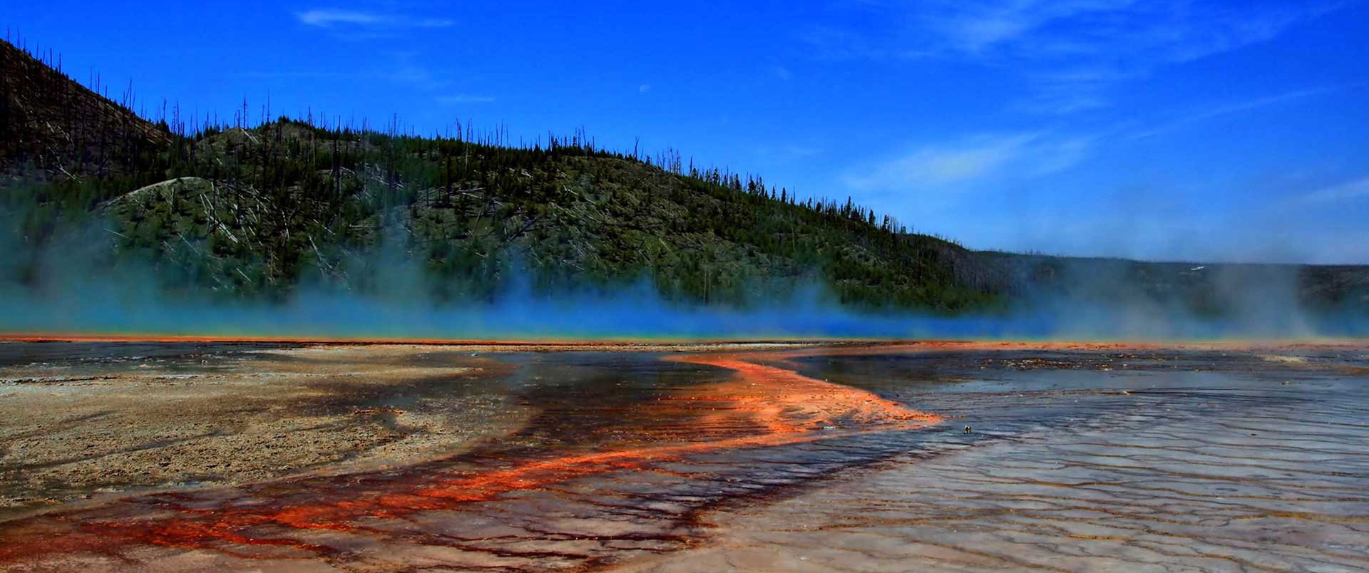The Grand Prismatic Spring of Yellowstone National Park showing steam rising from hot water, which is surrounded by huge mats of brilliant orange algae and bacteria
