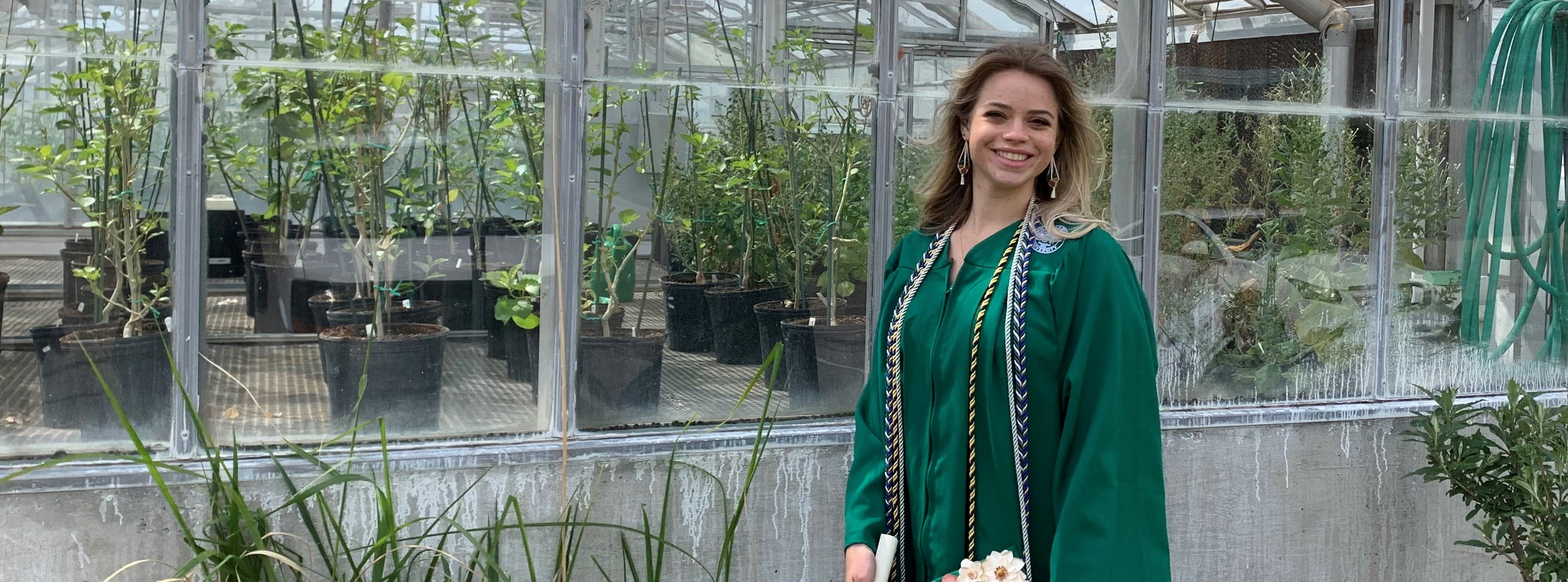 Kaylie Barton in her graduation gown outside of a greenhouse