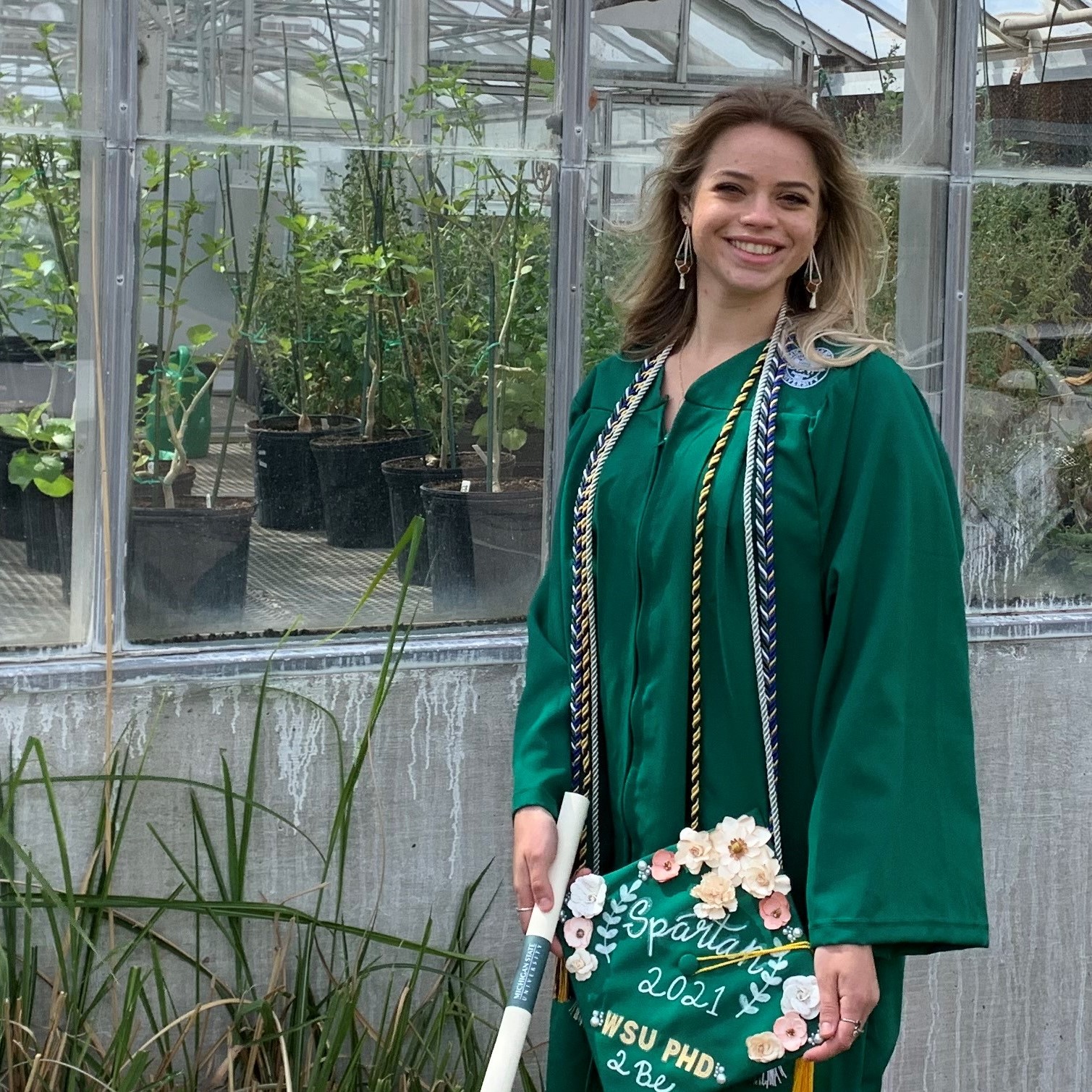 Kaylie Barton in her graduation gown outside of a greenhouse
