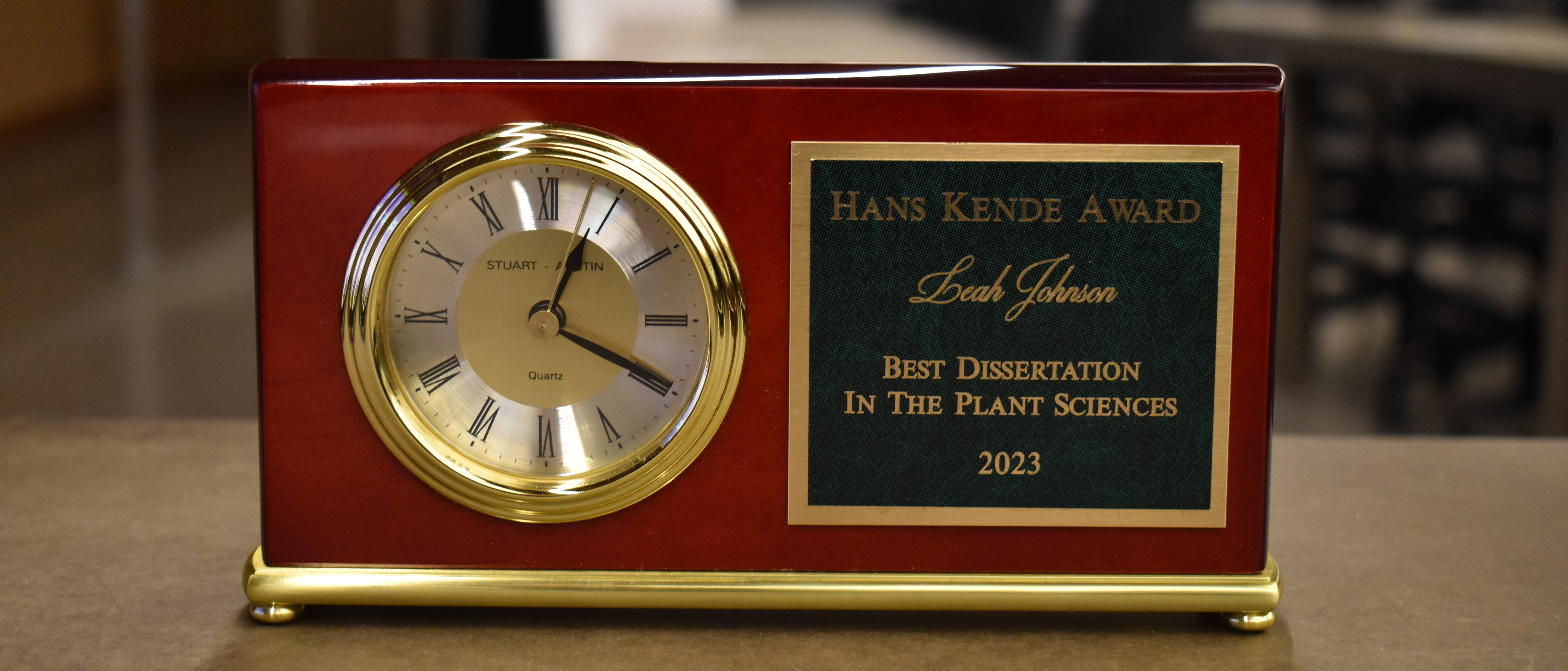 A clock with a plaque with text that reads: Hans Kende Award. Leah Johnson. Best Dissertation in the Plant Sciences 2023