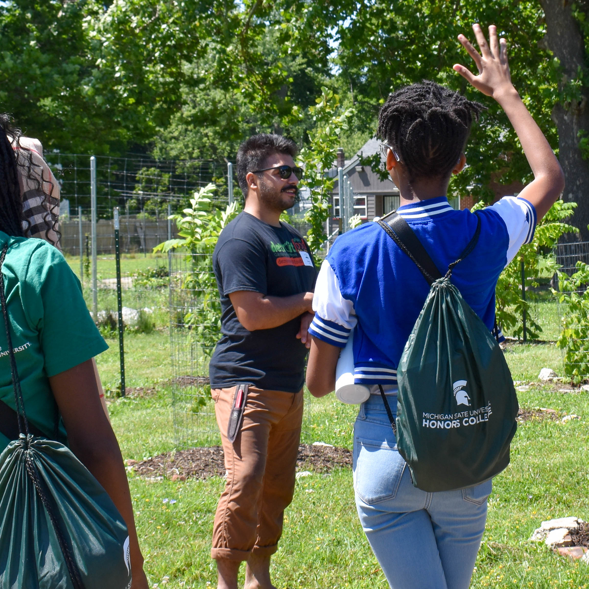 A person presents outside, another raises their hand. They are wearing a backpack that states 