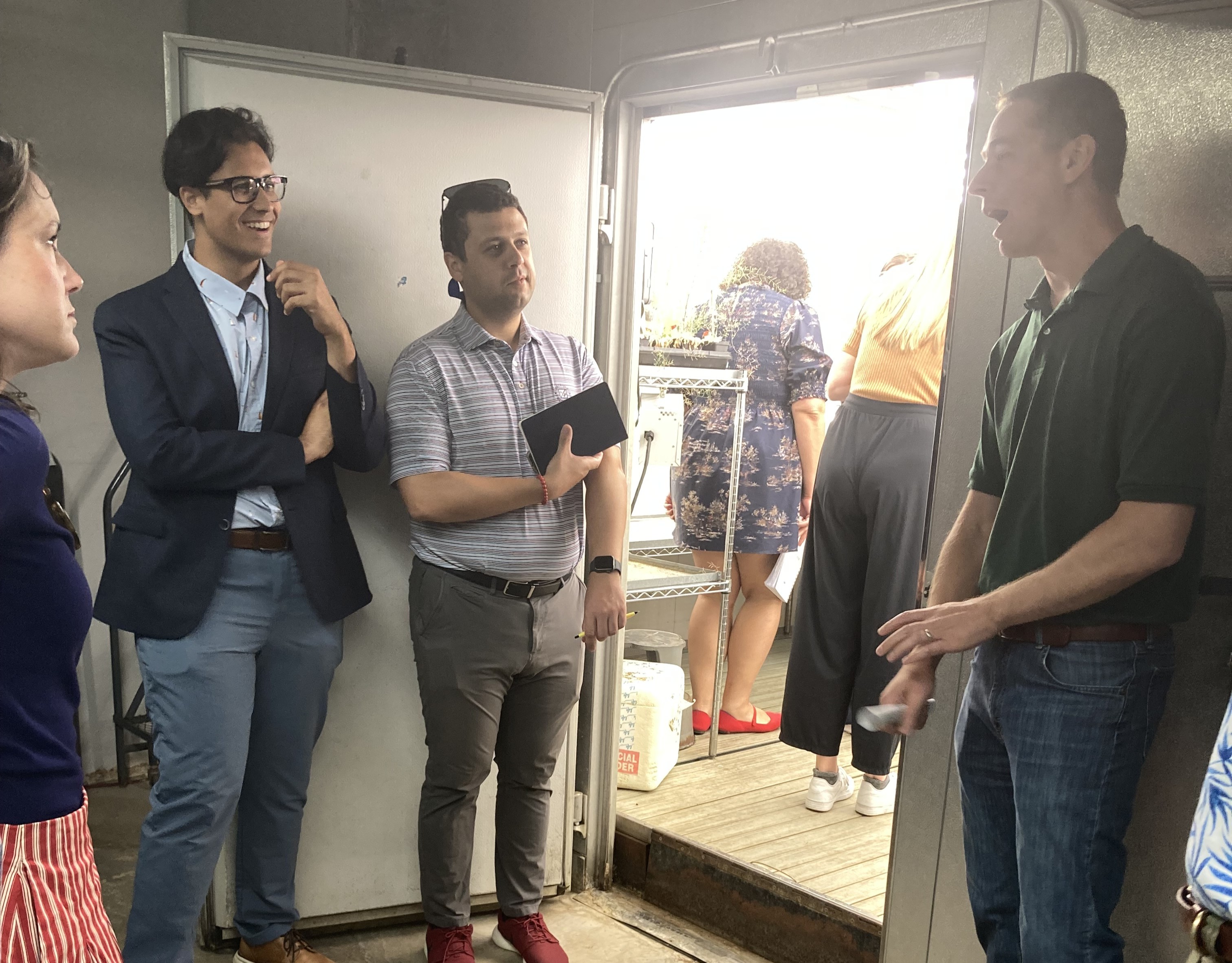 People talk in front of a growth chamber, a large machine that houses plants