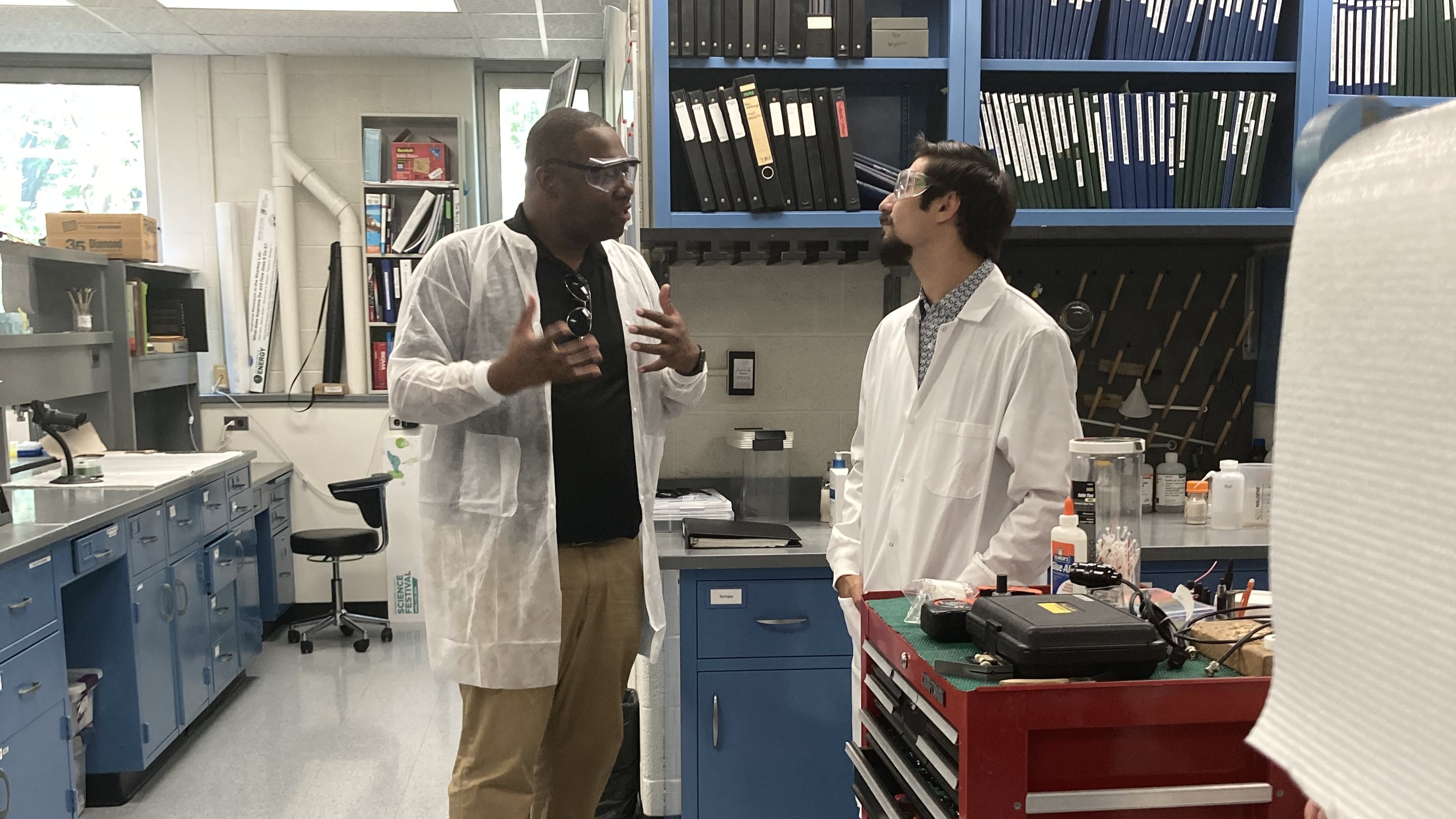 Two people in lab coats talk in a lab